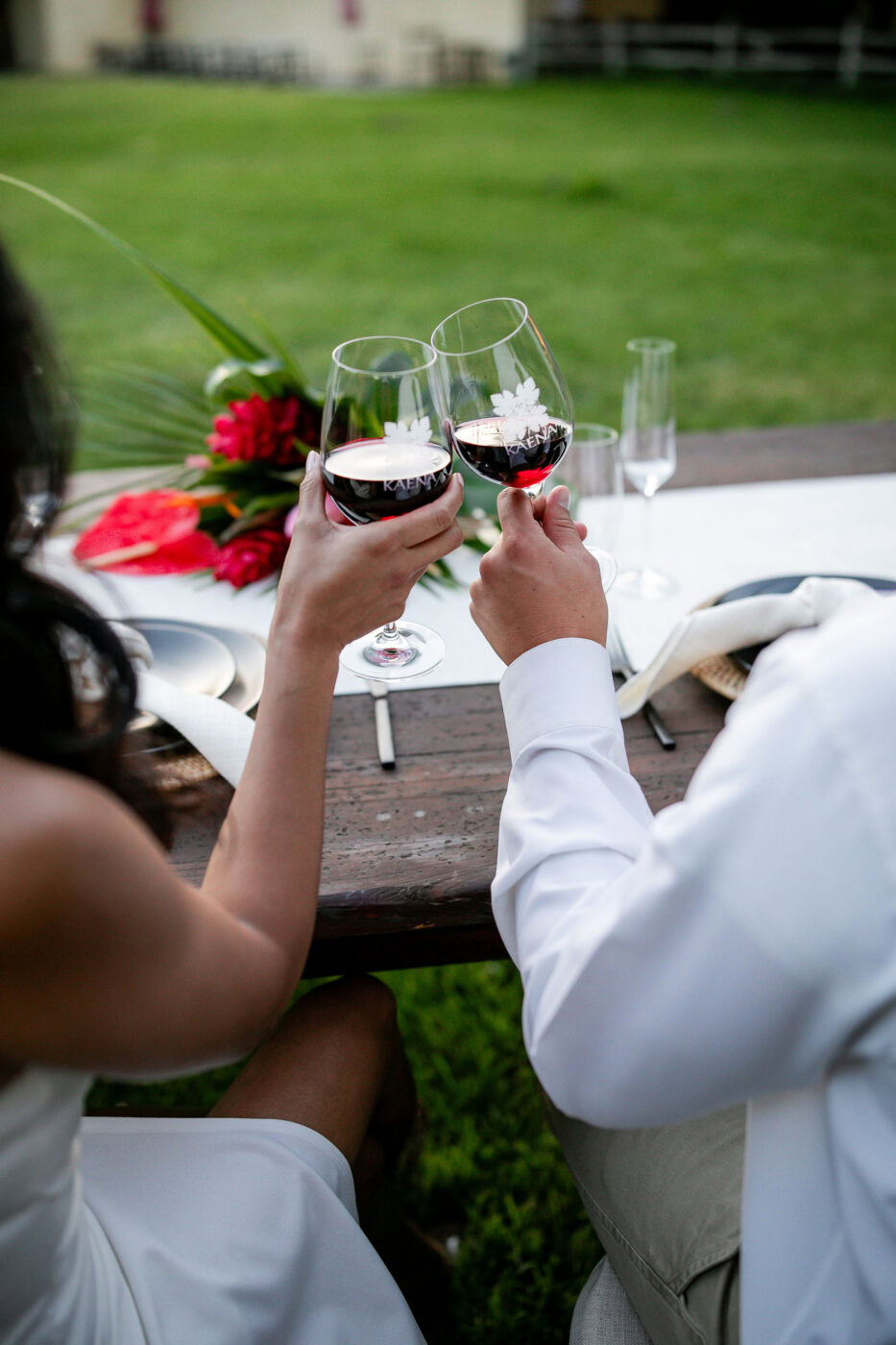 A woman and a man clinking glasses of red wine at an outdoor table during a private event.
