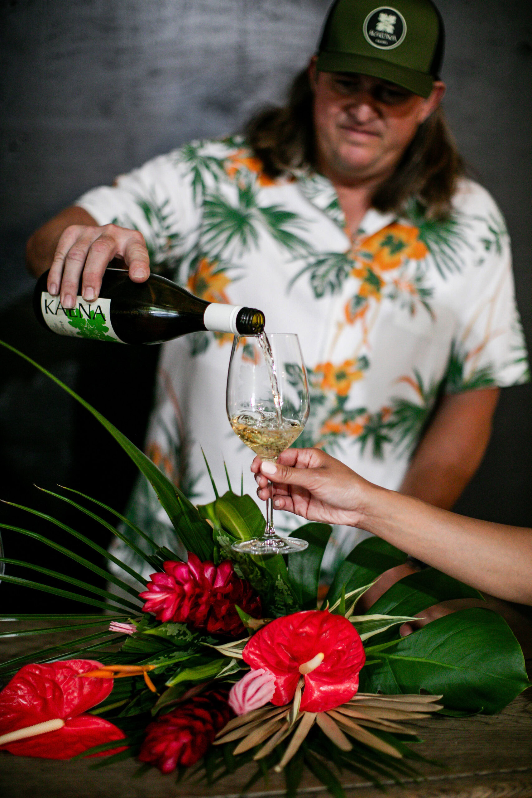 Kaena Wine Co. pouring wine into a glass at a tropical-themed setting.